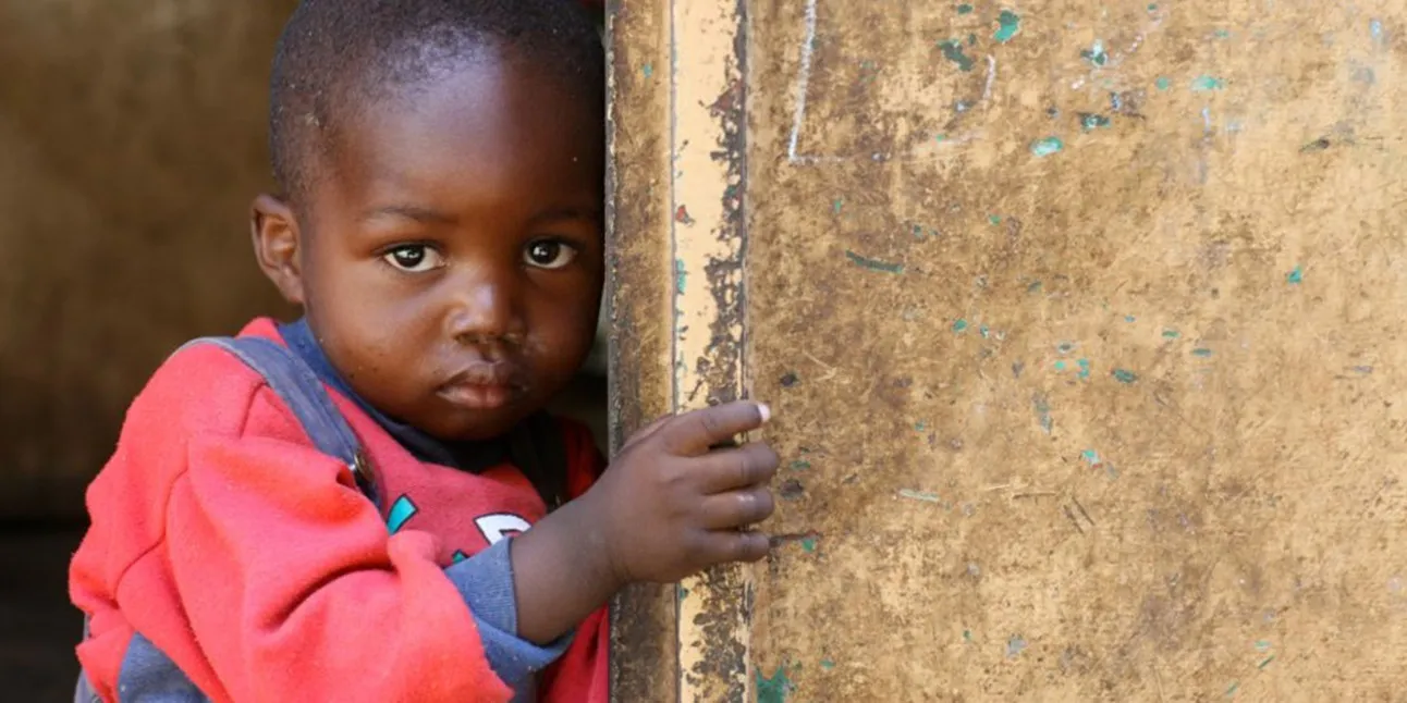 Un jeune enfant regardant l'objectif, adossé à une porte